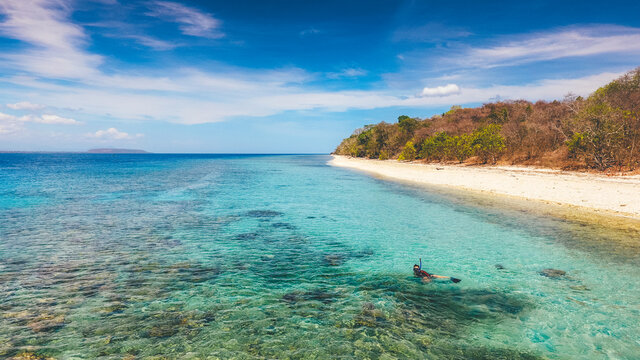 Aerial drone view of an empty white sandy beach with a man snorkeling in tropical Moyo Island, Sumbawa, Indonesia