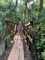 Naklejka na ściany i meble Young Girl hiking in a forest and walking over a bridge