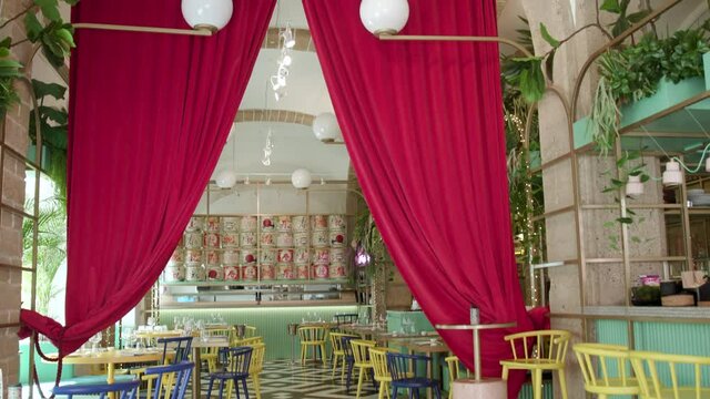 Wide shot of a restaurant with Twin peaks theme. A black and white chevron zig zag floor and red curtains are in the background. Yellow and blue chairs.