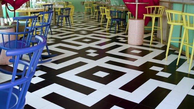 Zoom in. Restaurant with Twin peaks theme. A black and white zig zag chevron floor and red curtains are in the background. Yellow and blue chairs.
