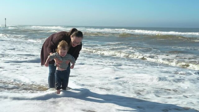 Mother and son playing at the beach on a windy summer day with big white foam waves crashing