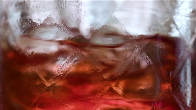 Super slow motion, macro of a cocktail glass, half full with red bitter and half empty. Detail of the bar spoon mixing the drink.