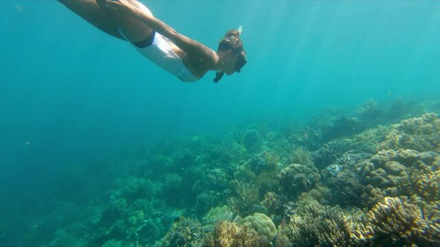 Slow motion panning shot of young woman snorkeling over coral reef in ocean - Wakatobi Regency, Indonesia