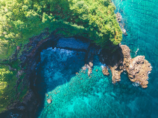Aerial view of rocky hill coast with green trees and blue sea with white foaming waves in Nipah Hill, Lombok Island, Indonesia