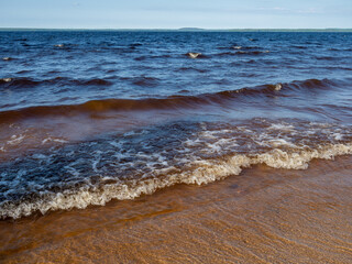 Waves with white foam on a lake with shallow depth in a sunny, windy day in Karelia, northwest of Russia