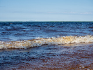 Waves with white foam on a lake with shallow depth in a sunny, windy day in Karelia, northwest of Russia