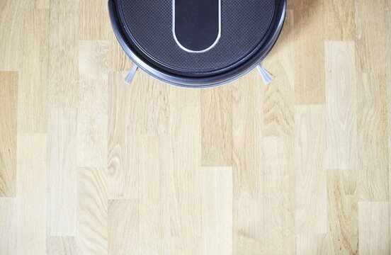Overhead Shot Of A Black Robot Vacuum Cleaner On A Light Wooden Parquet Floor