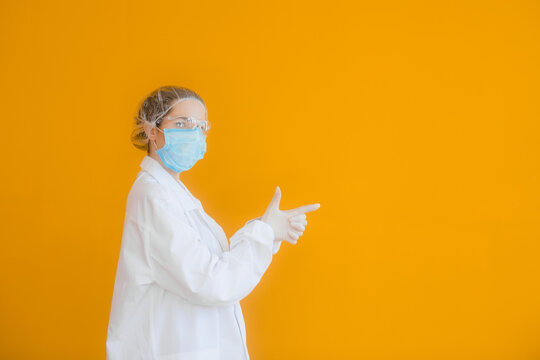 Portrait of a doctor, a young woman in a protective medical mask on her face and a cap on her head. looking seriously into the frame. on a yellow background. surgeon. ambulance paramedic. copy space