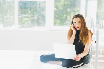 One young woman of 25 years of European appearance lies on a bed with a laptop at home on a white bed. Feels an unhealthy headache or eye strain, bad news