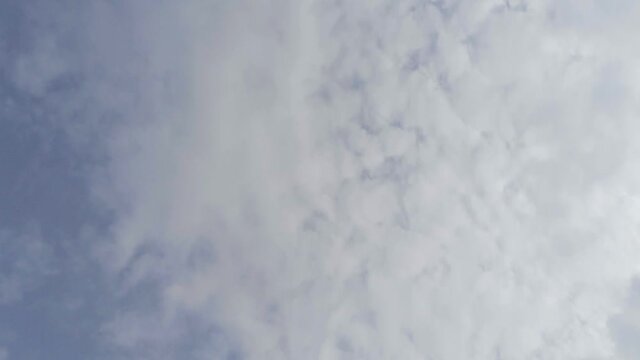 Light wispy hazy high cirrus stratus clouds floating past a powder blue background sky, aerial