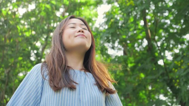 Slow motion of Asian girl breathe deeply in a green park to enjoy the beauty and purity of nature.