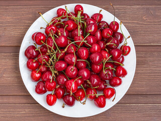 juicy red ripe fresh cherries in a white plate on a wooden table