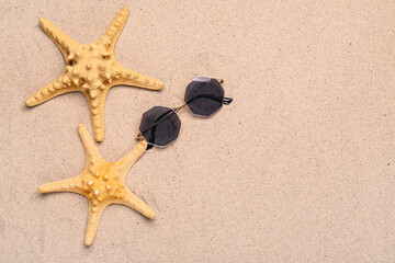 Fototapeta na wymiar Stylish sunglasses with starfishes on sand background