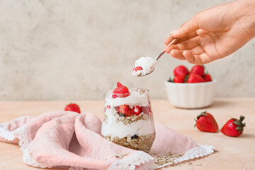 Woman eating tasty strawberry dessert in glass on table