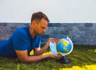 Man wearing Face Mask holding the Earth globe world map in hand. Quarantine yourself to protect...