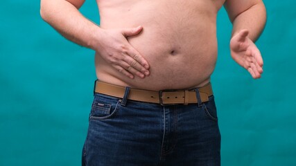 Naklejka premium male with a big belly shows his fat on a green screen. The concept of healthy eating and losing weight, diet