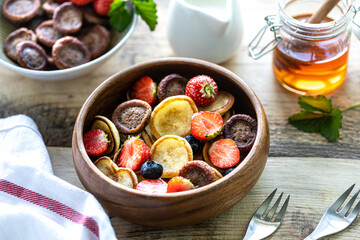 Different mini pancakes in a wooden bowl with honey, milk and blueberries on a wooden table. Trendy food