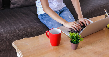 Asian woman is using a notebook computer and sitting on a sofa for working from home. 