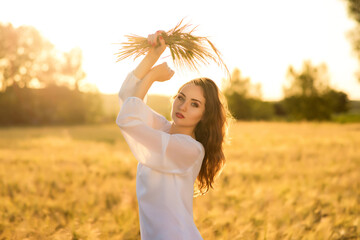 Beautiful young woman wearing white dress in wheat field relaxing. Glow sun