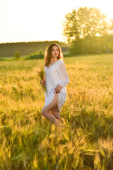 Beautiful young woman wearing white dress in wheat field relaxing. Glow sun