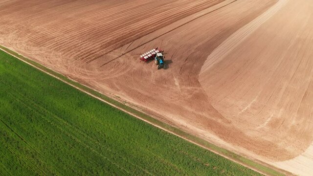 Aerial view of tractor with mounted seeder performing direct seeding of crops on plowed agricultural field. Farmer is using farming machinery for planting process, top view