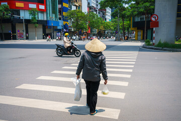 Vietnamese woman with conical hat walking on crosswalk in Hanoi