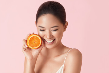 Beauty. Woman And Fruit Portrait. Happy Asian Model Holding Juicy Orange Near Face And Looking Down On Pink Background. Beautiful Ethnic Girl Uses Citrus And Natural Vitamins For Healthy Skin.