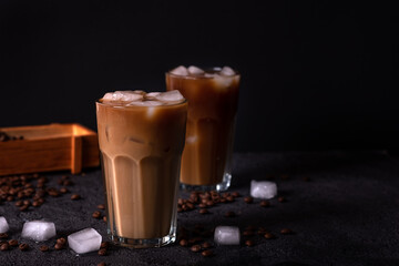 Iced coffee in a tall glass with cream poured over. Wood background. Low key.
