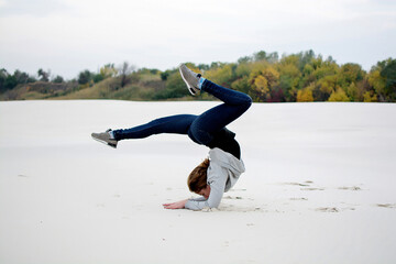 A young girl goes in for sports on the beach. Acrobatics. Young woman performs yoga exercises
