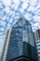 Obraz premium Closeup of top modern high-rise modern buildings. Mirroring of concrete skyscrapers on blue sky in shiny glass windows.