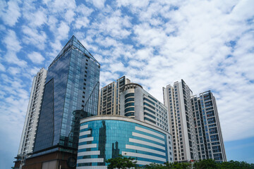 Fototapeta premium Closeup of top modern high-rise modern buildings. Mirroring of concrete skyscrapers on blue sky in shiny glass windows.
