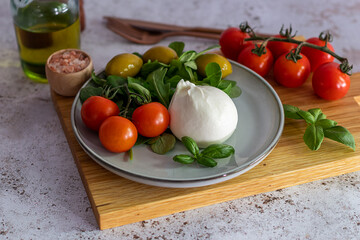 Delicious fresh Italian burrata cheese on a light plate with tomatoes, basil and olives. Close up. Selective focus