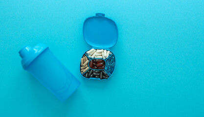 Container with daily supplements with blue sport shaker. Top view of container for pills. Healthcare and sport concept with copy space.