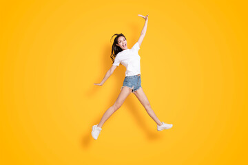 Fototapeta na wymiar Happy young woman jumping and looking at the camera over yellow background