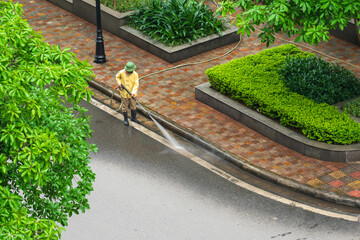 Aerial view of park with worker cleaning dirty street with high pressure cleaner