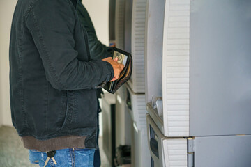 Asian man standing in front of an ATM machine, withdrawing money