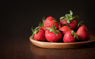 Fresh strawberries on a wooden plate against black background