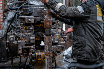 Two working drillers in a uniform, in a helmet and goggles, install drill pipes after lifting them from an oil well after drilling. The concept of a working person.