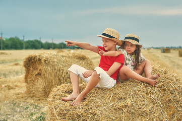 Naklejka na ściany i meble Happy children at the haystack . Happy childhood, brother and sister on a walk