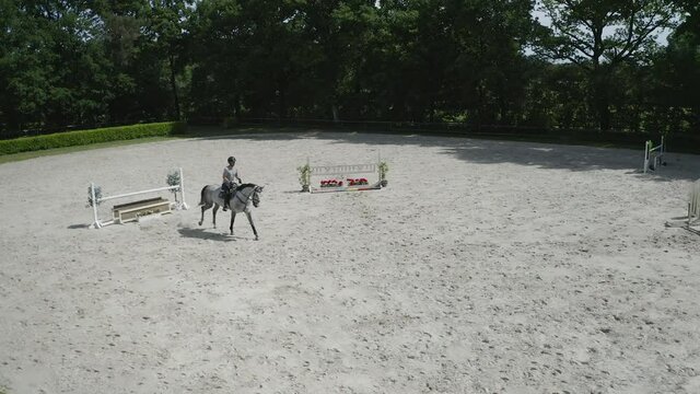 Pferd springt &uuml;ber Hindernis. Drohne verfolgt jungen Reiter. Sandplatz Parkour. Sprung