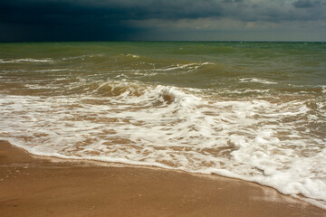 Thunderstorm over the ocean. A big waves is approaching an empty beach. Horizontal photo.