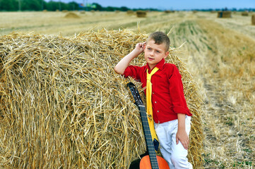 Portrait of a boy with an acoustic guitar in a field near a haystack