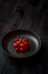 dark red and fresh cherries in a black ceramic bowl on wooden background with selective focus