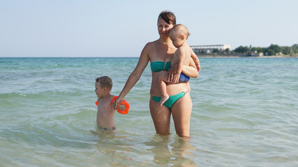 Young mother standing in water in sea with two little boys