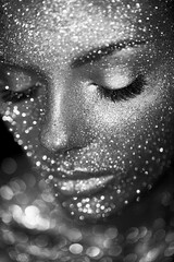 Fashion model woman in bright sparkles and lights posing in studio. Portrait of beautiful sexy woman. Art design glitter glowing make up. Black and white photography