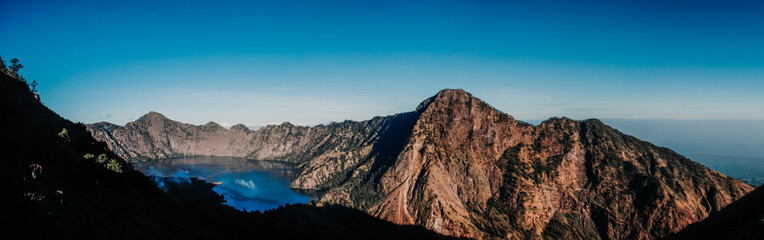 Panorama view of Segara Anak Lake in Mount Rinjani, Lombok, Indonesia. Sunny afternoon. wonderful springtime landscape in mountains. grassy field and rolling hills. rural scenery