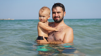 Fototapeta na wymiar Little happy kid and his smiling father in sea. Dad holding boy