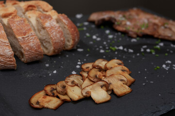 mushrooms on top of a piece of slate, bread and meat in the background
