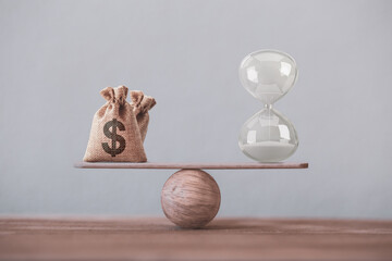 Financial concept : Write sand clock or hourglass symbol and dollar bagson a balance scale in equal position.Time value of money, asset growth over time, investment in long-term equity for more money  - obrazy, fototapety, plakaty
