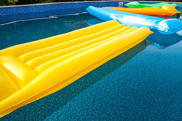 Multicolored air mattresses floating on the calm surface of a smaller pool in the garden of a house...